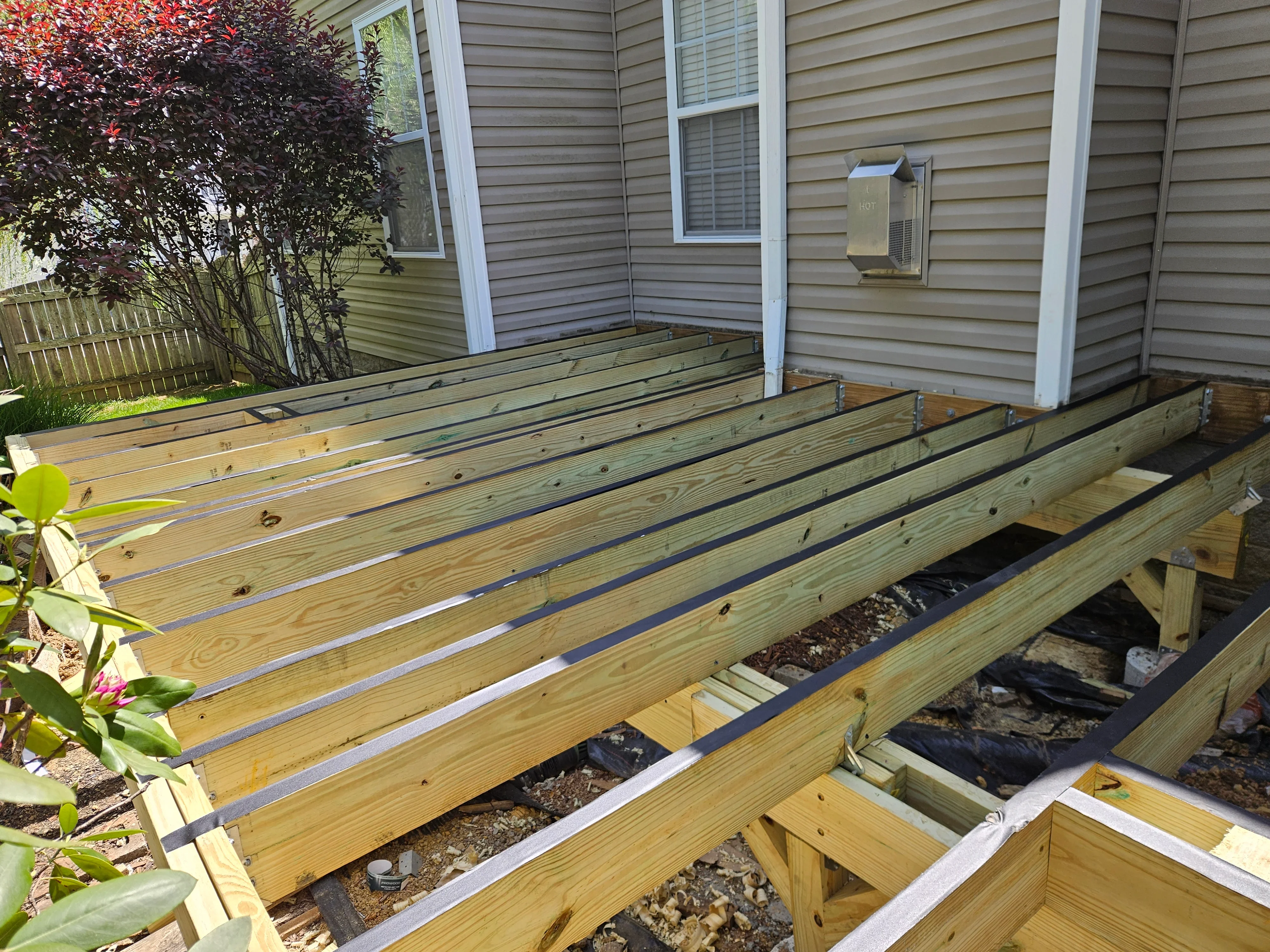 Pressure-treated wood deck framing with joists, beams, metal flashing, and landscape fabric on concrete piers