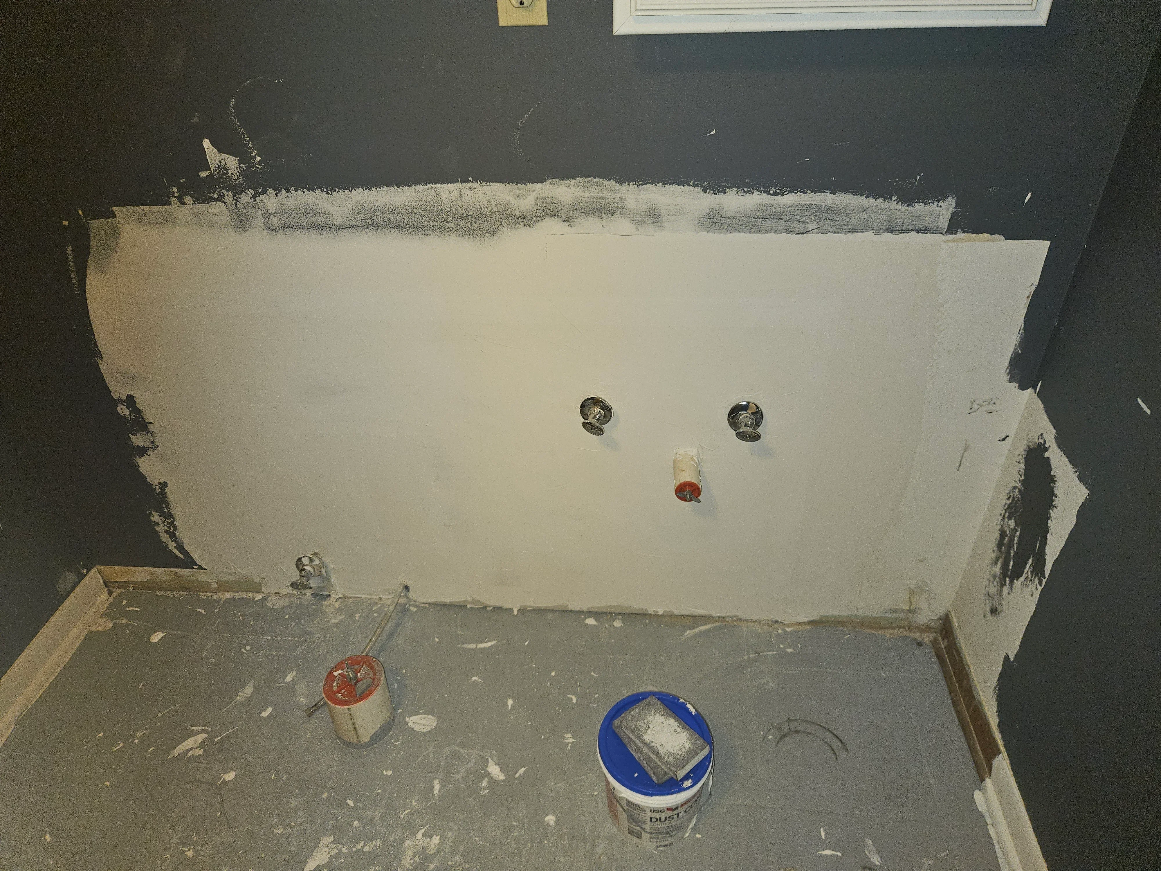 Drywall sheets installed on walls with joint compound, electrical boxes, and finishing materials visible