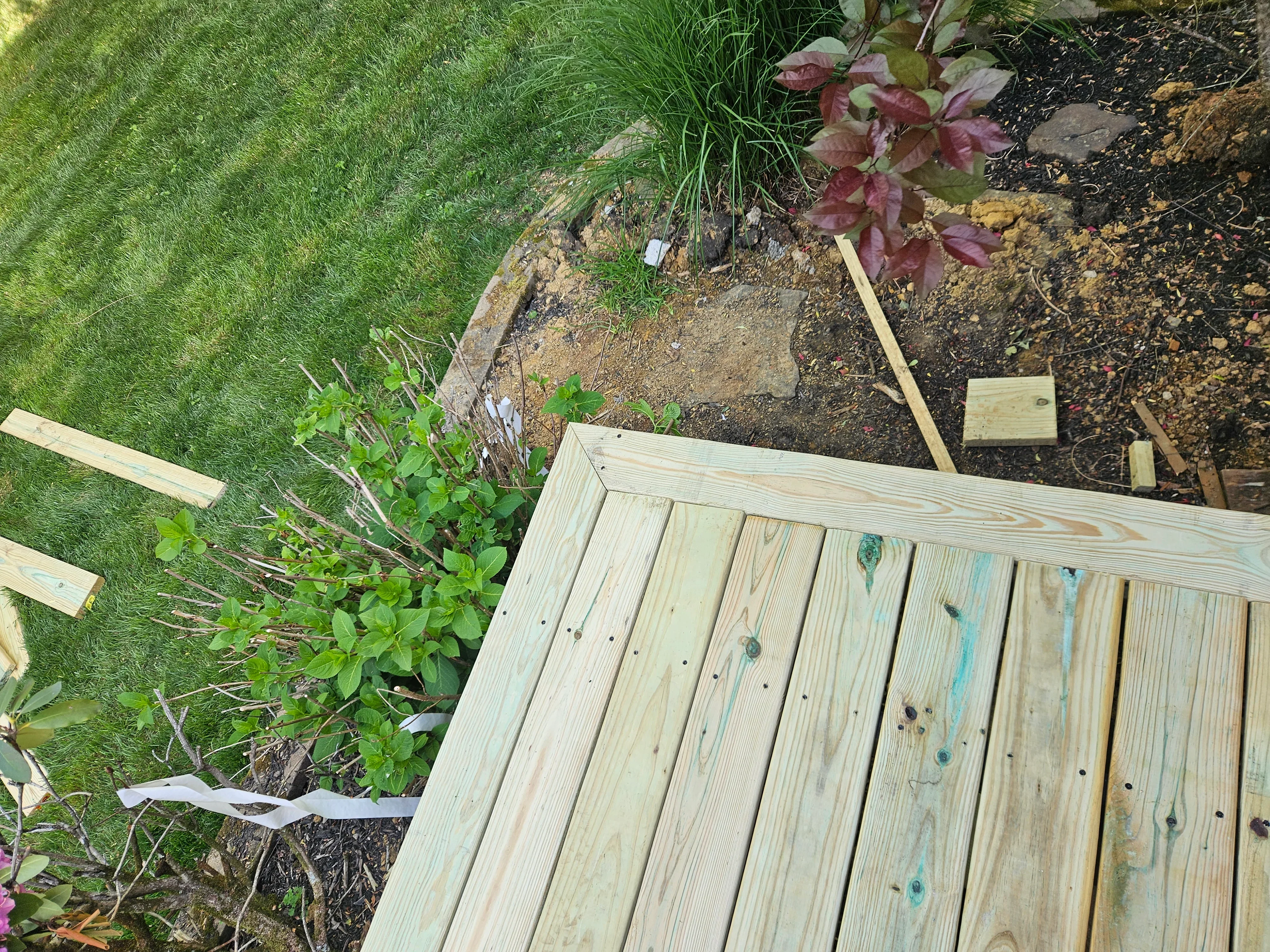 Pressure-treated wood deck with dimensional lumber boards adjacent to lawn and garden beds