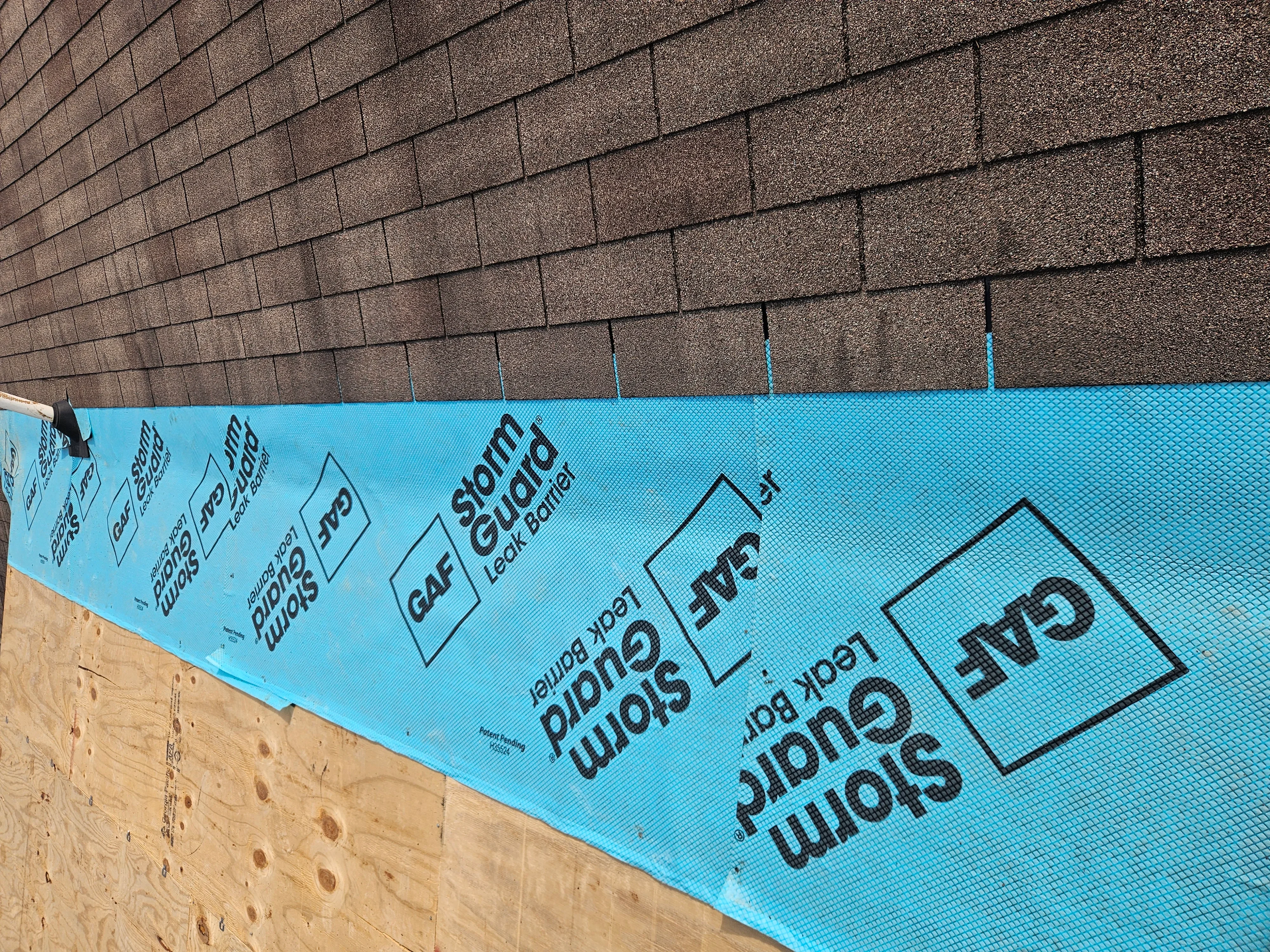 Blue synthetic roof underlayment installed over plywood sheathing with fasteners and asphalt shingles above